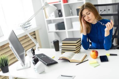 一个年轻的女孩坐在电脑桌前, 手里拿着眼镜, 揉着眼睛。在女孩躺在一本开放的书和一个苹果之前