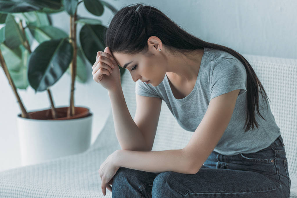 沮丧的年轻妇女在消沉坐在沙发上往下看
