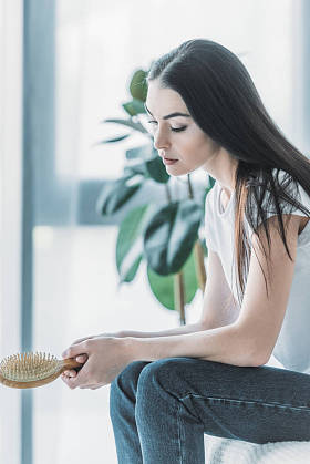 年轻的伤心女人坐在室内的梳子, 脱发概念的侧面视图