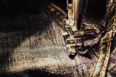 在缝纫机上修牛仔裤。织物, 针和螺纹的看法。内置白炽灯照明。牛仔裤是一种裤子, 通常是用牛仔布或 dungaree 布料制成的