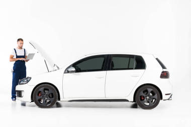 英俊的汽車技工使用筆記本電腦附近打開汽車罩白色