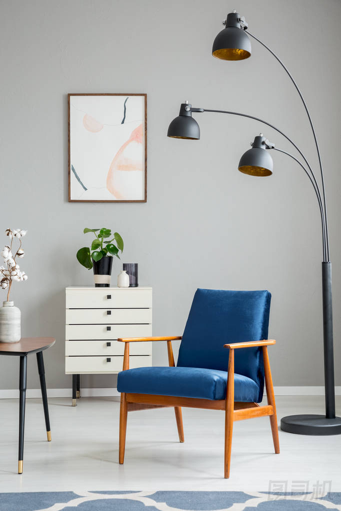 黑燈旁邊的藍色木扶手椅在灰色公寓內(nèi)部與海報和植物。真實照片