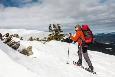 一個人爬上山頂。登山運動員在雪地鞋背著一個背包。在冬天的山上旅行。大自然中的極端假期。極端條件下的旅游者