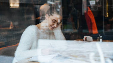 可愛的女孩在白色毛衣和眼鏡坐在咖啡館, 學(xué)習(xí)后休息