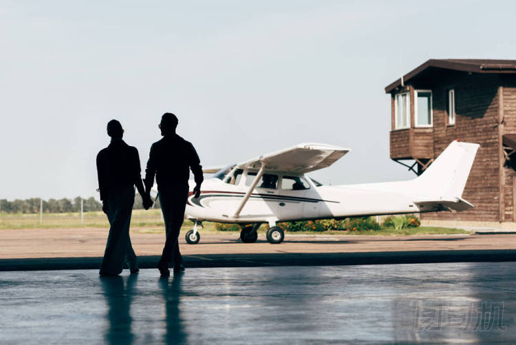 時尚情侶牽手和步行在飛機機庫附近的剪影后視圖