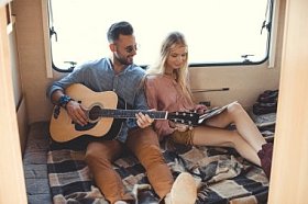 快乐的男朋友玩吉他, 而女朋友持有乙烯基记录内 campervan