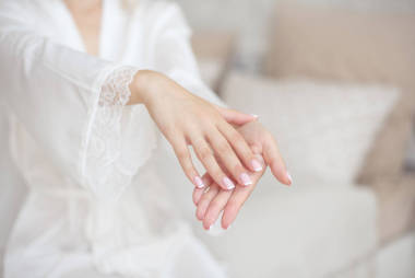 特写女性手集中与模糊苗条的腰部身体在背景。穿着婚纱的女人握着她的手在她的特写镜头前