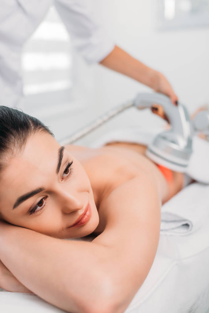 美丽的女人在按摩台上得到美容师在水疗沙龙进行的电按摩 美丽的女人在按摩台上得到美容师在水疗沙龙进行的电按摩