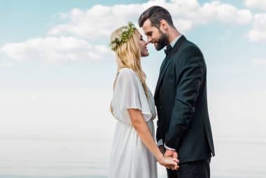 婚禮情侶西裝和白色禮服牽手, 觸摸與鼻子在海灘上