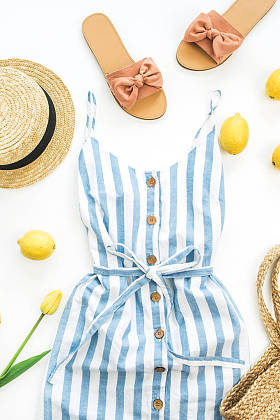 夏季女性时尚的构图。礼服, 拖鞋, 稻草, 柠檬, 郁金香花和配件在白色的背景。平躺, 顶部视图