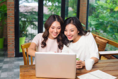 快樂的年輕女性朋友做網(wǎng)上購物使用筆記本電腦和信用卡坐在客廳