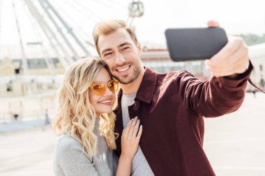 微笑的情侶在秋季服裝采取自拍智能手機在城