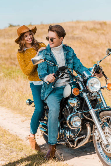 年輕幸福夫婦坐在復(fù)古摩托車在鄉(xiāng)村草地上