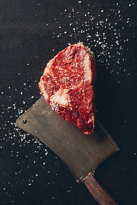 厨房内桌上生肉牛排、盐和切刀的顶部视图