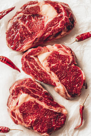 三塊生肉牛排和辣椒在廚房烘烤紙上的最高視圖