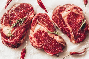 三塊生肉牛排, 辣椒和迷迭香在廚房烘烤紙上的最高視圖
