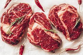 三块生肉牛排, 辣椒和迷迭香在厨房烘烤纸上的最高视图