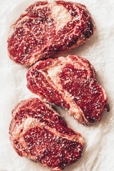 廚房烘烤紙上三塊生肉牛排加鹽的頂部視圖