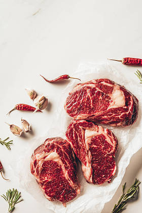 厨房烘烤纸上三块生肉牛排和蔬菜的最高视图