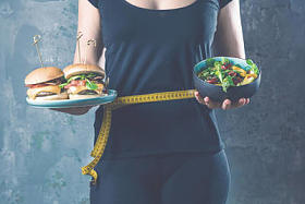 健康的年轻妇女持有健康和不健康的食物盘子, 试图做出正确的选择