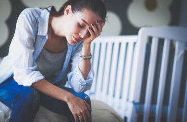 年輕疲憊的女子，坐在附近兒童床床上