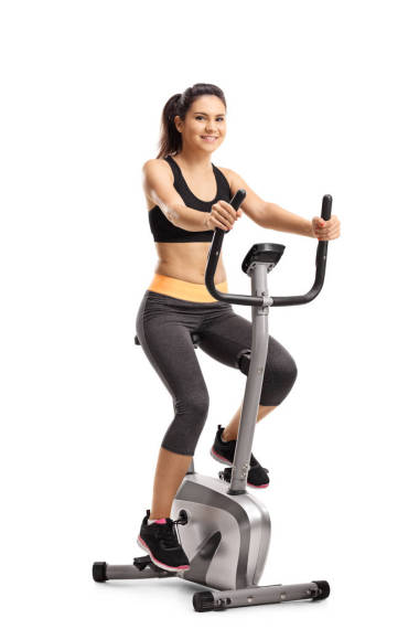 一個(gè)年輕女子的全長肖像騎在白色背景上的固定自行車隔離