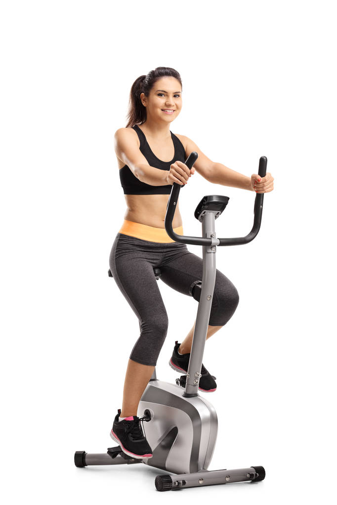 一个年轻女子的全长肖像骑在白色背景上的固定自行车隔离