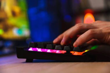 在家里坐在桌邊的玩家在電腦上玩電子游戲的裁剪圖像