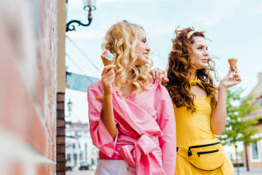 美麗的年輕婦女穿著時髦的五顏六色的衣服吃冰淇淋在街上