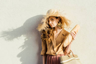 美麗的年輕女子草帽與面包站在白色的墻前, 看著相機(jī)