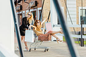 快乐时尚的年轻女子在购物时骑购物车在一起