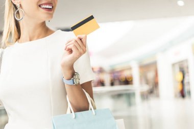 在购物中心拿信用卡的微笑的年轻妇女被裁剪的射击