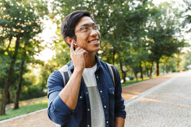 微笑的亞洲男性學生在眼鏡和耳機聽音樂, 而看著遠離