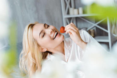 穿著睡衣的漂亮女人早上睡在床上吃草莓, 閉著眼睛