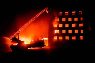 在夜里撲滅一棟私人房子的大火。玩具消防車與長的梯子和燃燒的建筑物在夜間。火警警報(bào)概念。選擇性聚焦