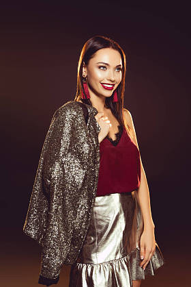 开朗的年轻女子在魅力礼服摆在肩上的夹克在黑色与背光