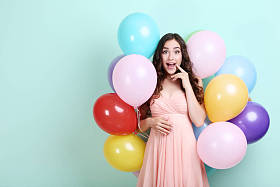 惊喜的年轻女孩粉红色的礼服与彩色气球站在薄荷背景