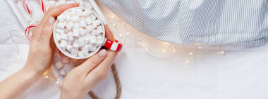 新年或圣诞节平躺顶部视图与热可可咖啡巧克力与棉花糖杯在妇女手圣诞节节日庆祝在木托盘在床上与灯。长宽横幅2019