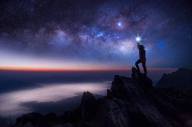 登山者或背包客剪影。在他的手里, 他把灯高高地举在头顶上。站在落基山脉山顶和银河, 成功, 赢家, 领导理念。高 iso 噪声