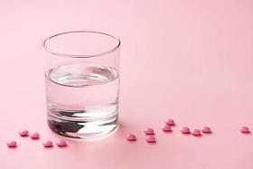 在粉红色的玻璃水和医用片剂特写视图  