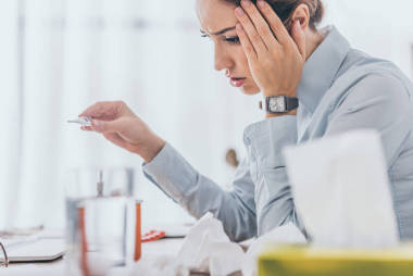 生病的女实业家坐在工作场所和手持电温度计