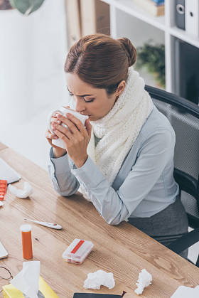 高视角的病态女实业家在围巾坐在办公室喝茶