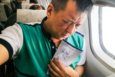 痛苦的亚洲人持有空气疾病呕吐袋在飞机机舱