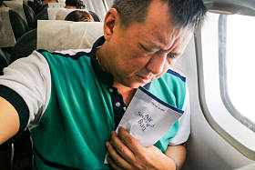 痛苦的亚洲人持有空气疾病呕吐袋在飞机机舱