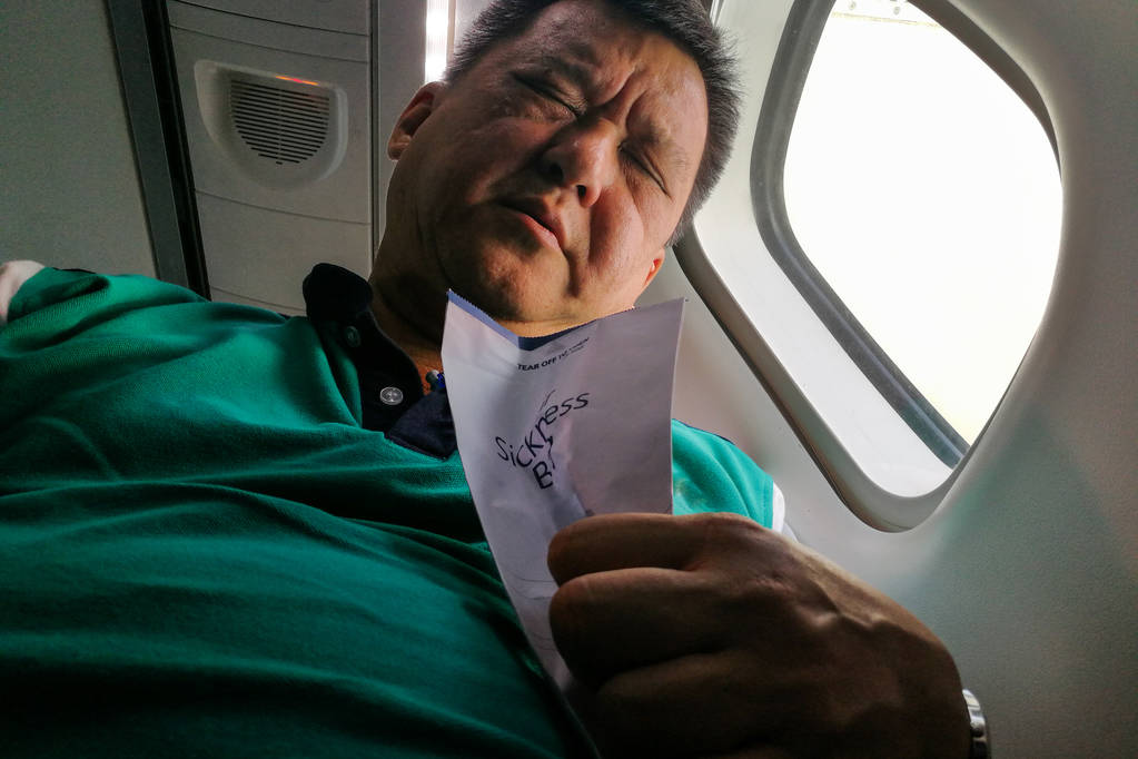 痛苦的亚洲人持有空气疾病呕吐袋在飞机机舱