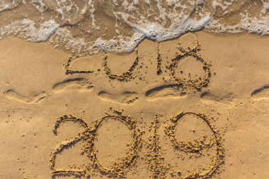 新年快乐2019的概念即将于2018年来临。海沙滩上的文字和沙子上的脚印。波浪水覆盖数字铭文。在泰国的热带度假胜地相遇