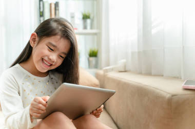 可愛的孩子使用平板電腦和微笑, 而坐在沙發(fā)上在家