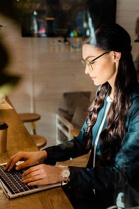 美丽的黑发 teleworker 在眼镜使用笔记本电脑在餐厅