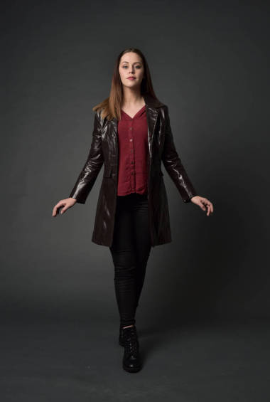 穿紅色長皮革插孔的黑發(fā)女孩的全長肖像。站在灰色工作室背景的姿勢