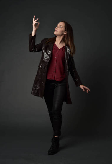 穿红色长皮革插孔的黑发女孩的全长肖像。站在灰色工作室背景的姿势
